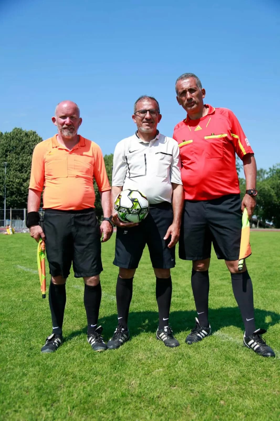 Les trois arbitres d’une rencontre du tournoi, ballon en main, sur la pelouse